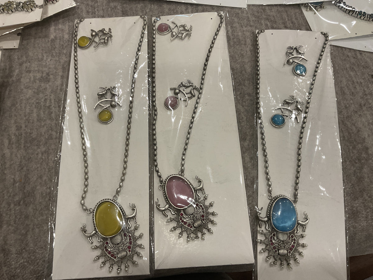Three silver-tone necklace designs in mustard yellow, pink and turquoise, with oval inserts, animal motifs and matching earrings.