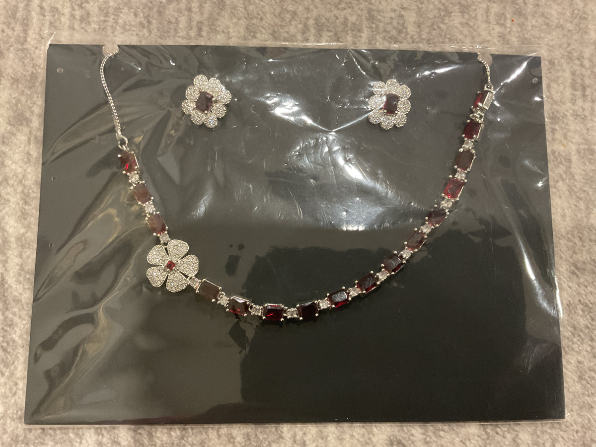 Deep-red necklace with white floral halo-shaped pendant detail and earrings displayed alongside