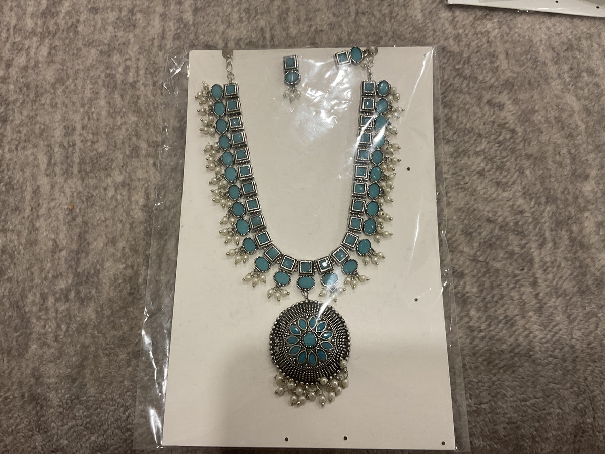 Silver-tone necklace and earrings with turquoise-blue inserts, a round floral pendant and off-white bead fringe.