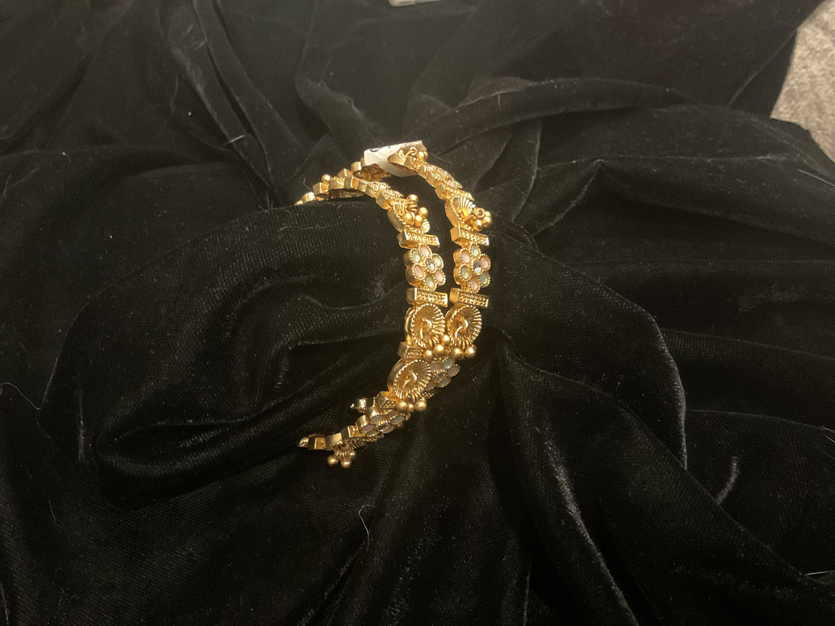 Two golden-colored bangles with floral motifs and small pale-pink accents.
