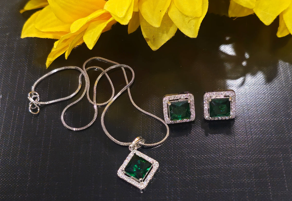 Silver-tone chain with square green halo pendant and two square stud earrings.