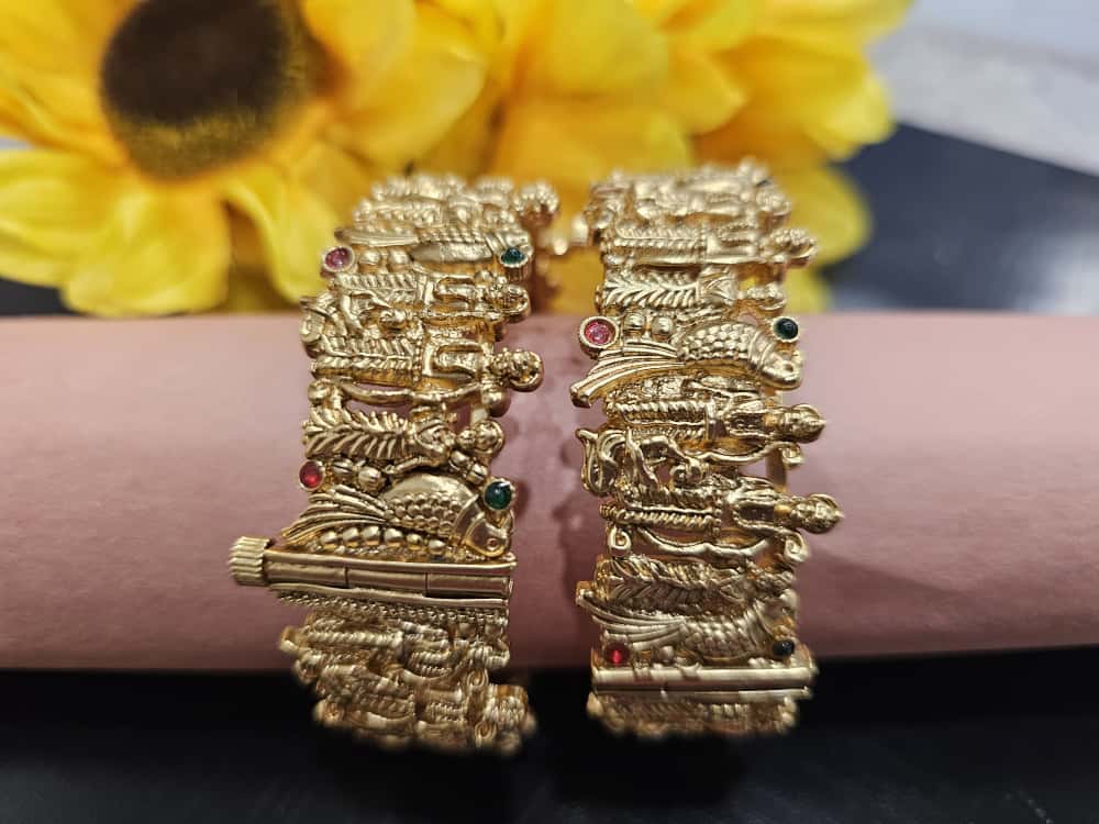 Pair of wide gold-tone bangles with sculpted figure/bird motifs and red/green accents.