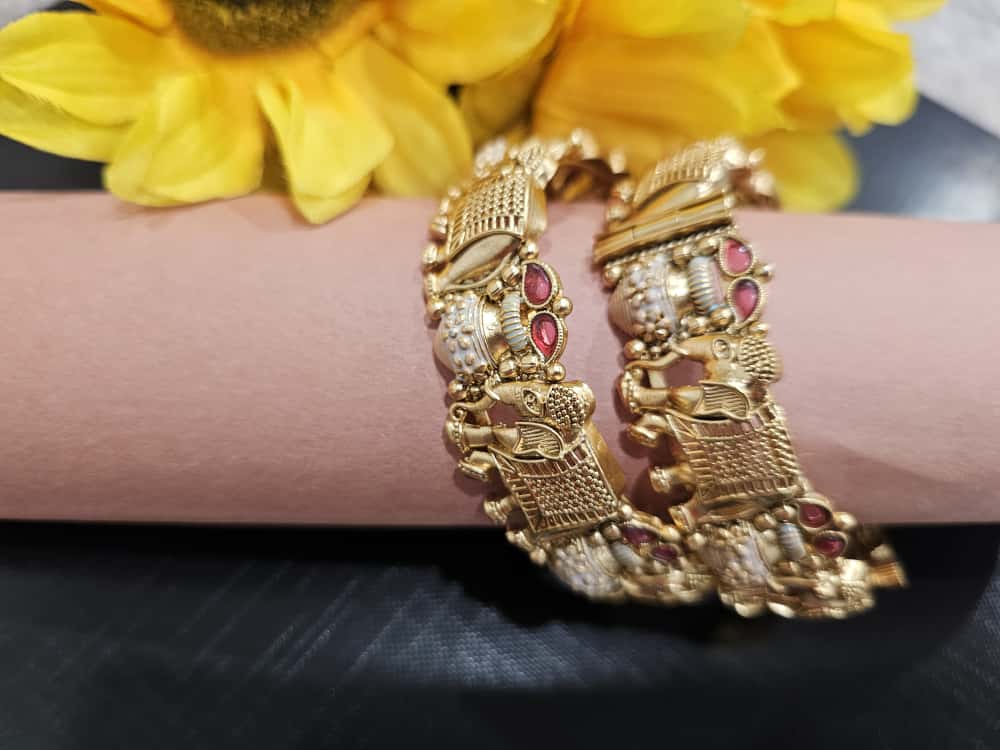 Pair of gold-tone bangles with bird motifs, pale panels and pink accents.