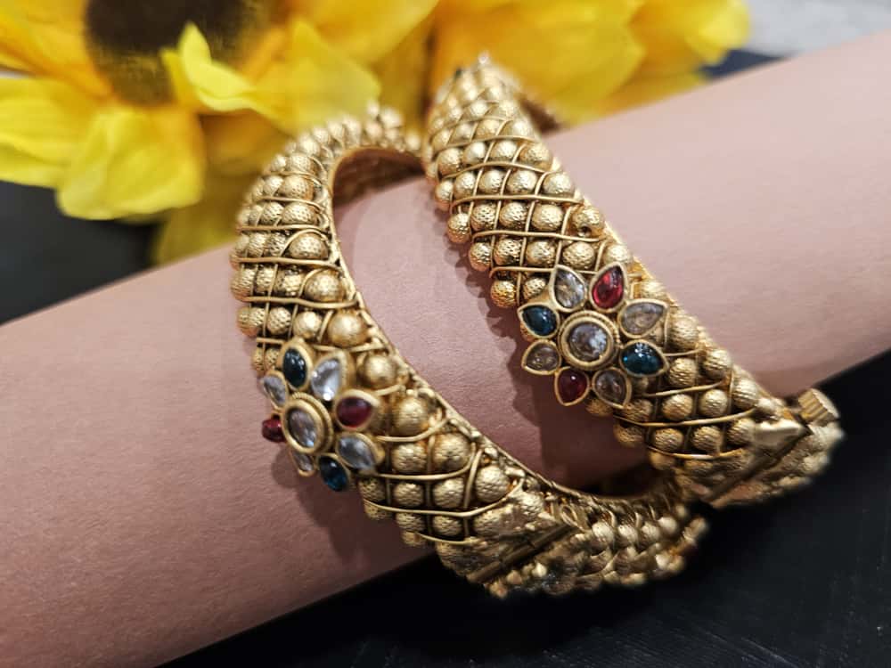 Pair of lattice-textured gold-tone bangles with multicolor floral center.