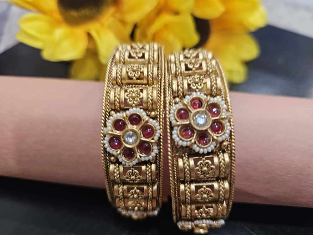 pair of gold-tone bangles with red-petal floral medallions and rectangular patterned bands.
