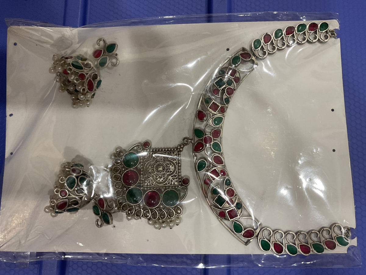 Silver-tone collar with red and green stones, decorated pendant and white bead fringe; necklace and two jhumka-style earrings shown.