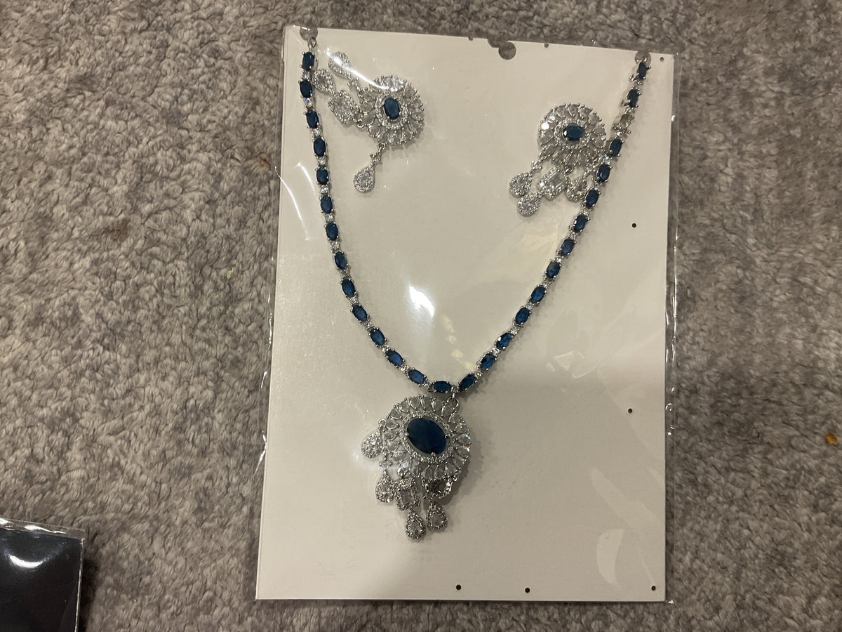 Navy-blue necklace with colored chain accents, a silver-tone oval-centered pendant, clear hanging drops and matching photographed earrings.