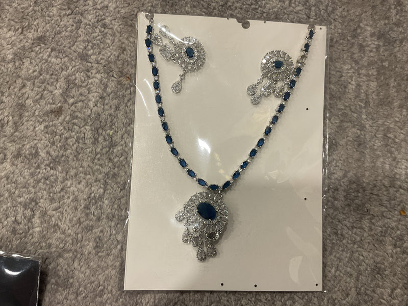 Navy-blue necklace with colored chain accents, a silver-tone oval-centered pendant, clear hanging drops and matching photographed earrings.