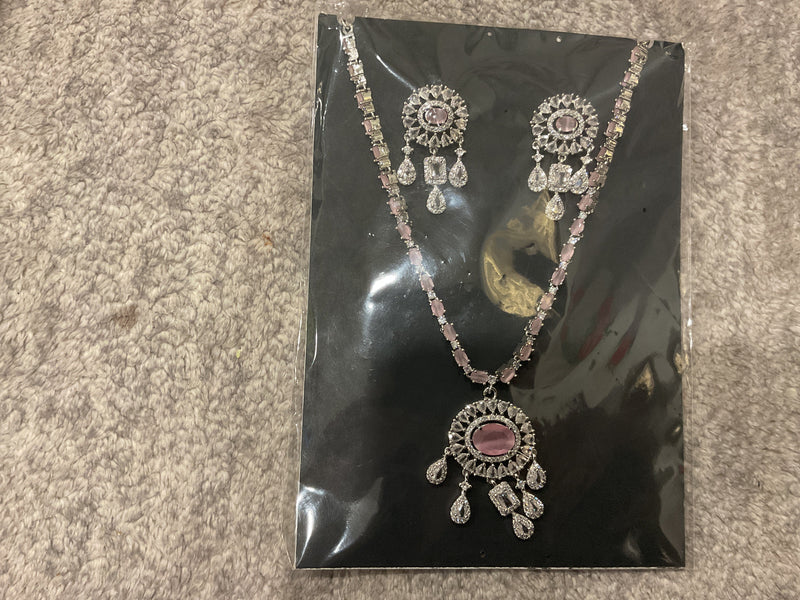 Baby-pink necklace with rectangular chain accents, a silver-tone oval-centered pendant, clear hanging drops and matching photographed earrings.