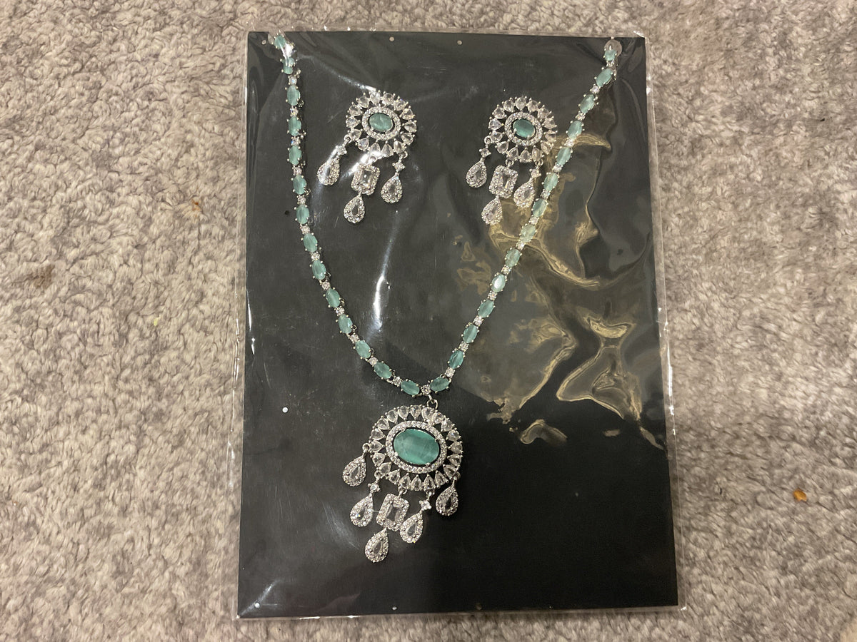 Mint-green necklace with colored chain accents, a silver-tone oval-centered pendant, clear hanging drops and matching photographed earrings.