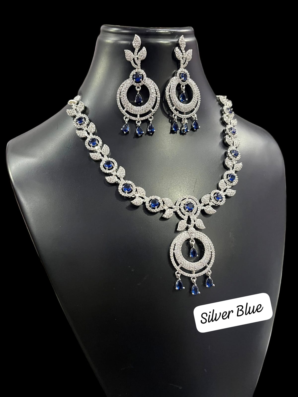 Silver-tone necklace and matching earrings with navy blue accents, leaf-shaped links, open circular pendants and dangling drops, displayed on a black jewelry bust.
