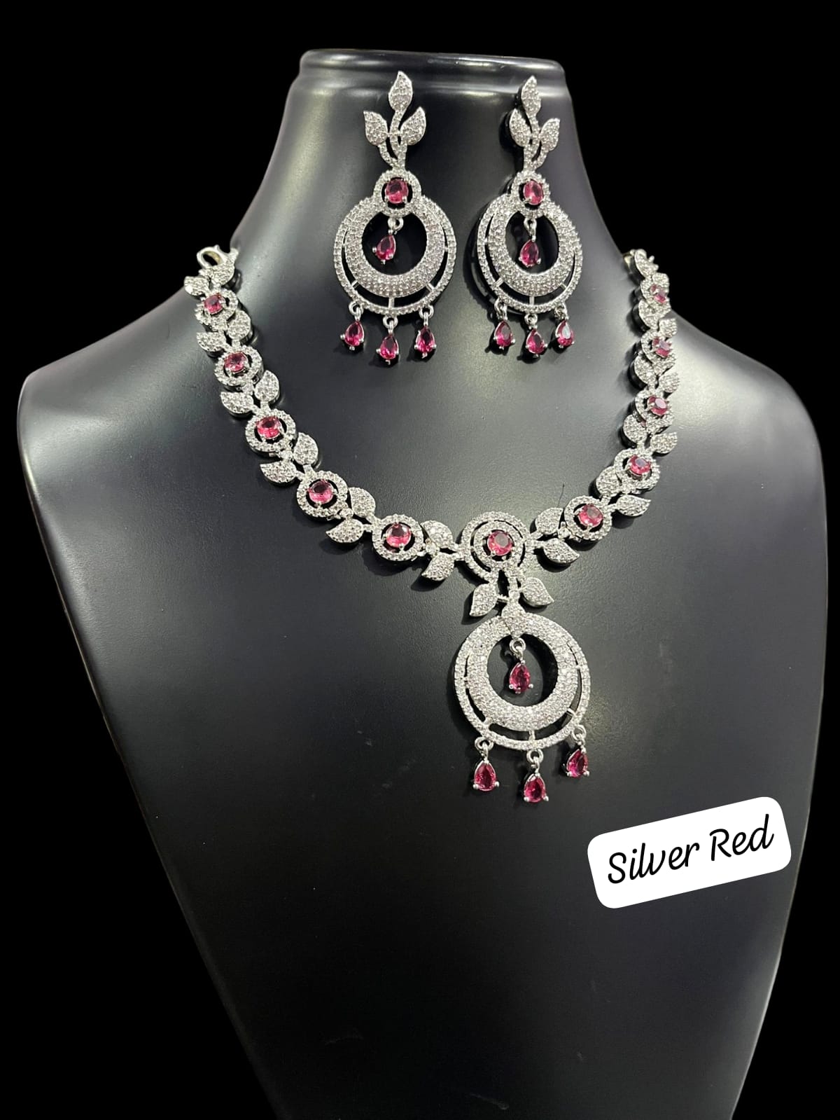 Silver-tone necklace and matching earrings with rani pink accents, leaf-shaped links, open circular pendants and dangling drops, displayed on a black jewelry bust.