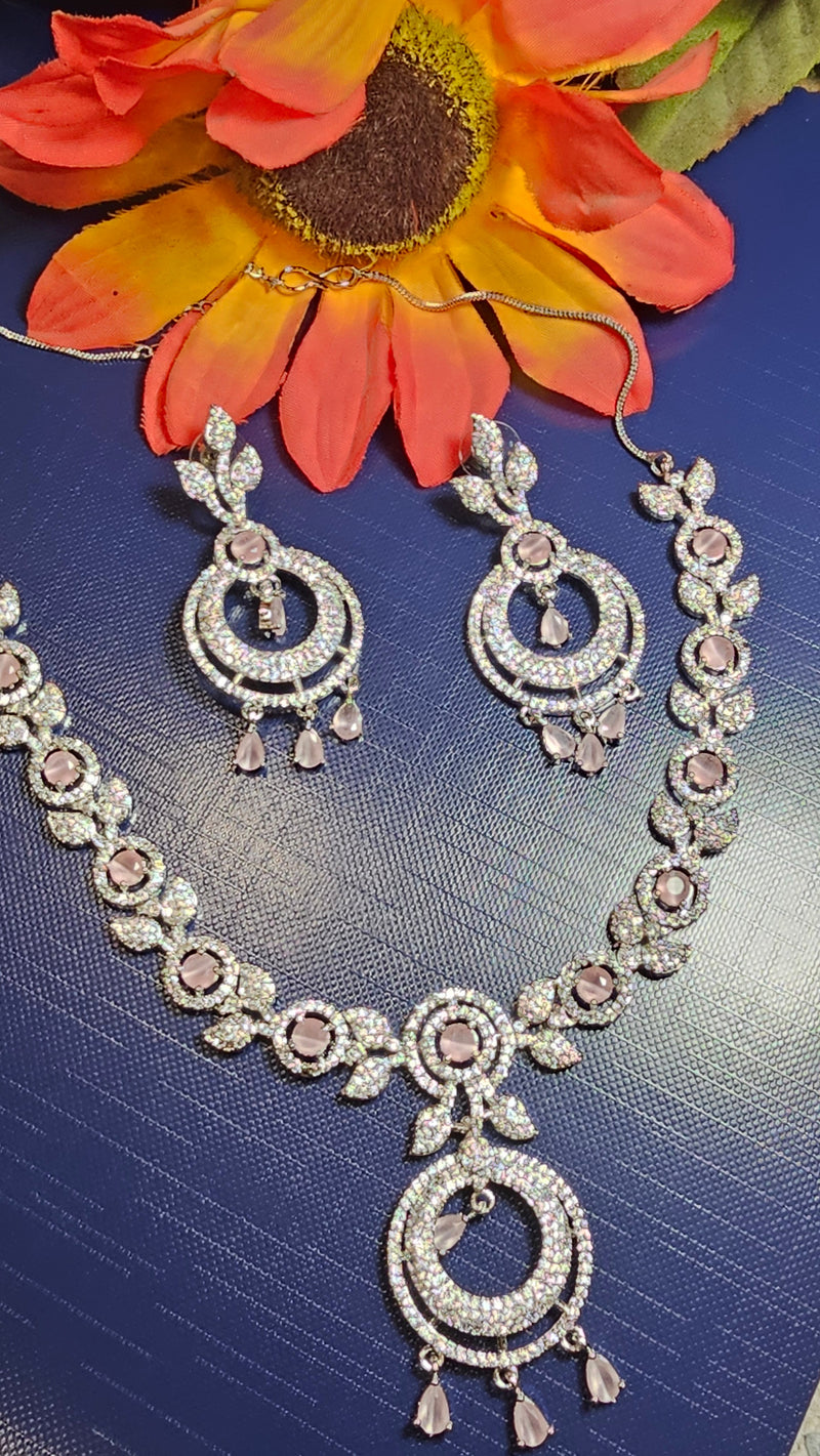 Silver-tone necklace and matching earrings with baby pink accents, leaf-shaped links, open circular pendants and dangling drops, arranged beside decorative flowers.