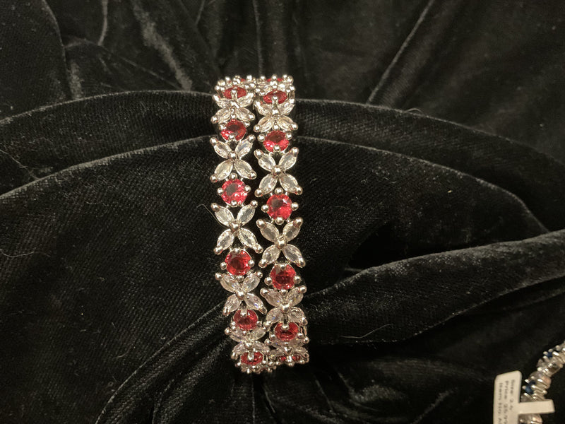 Two silver-tone bangles with rani pink round accents and clear leaf-shaped clusters on black fabric.