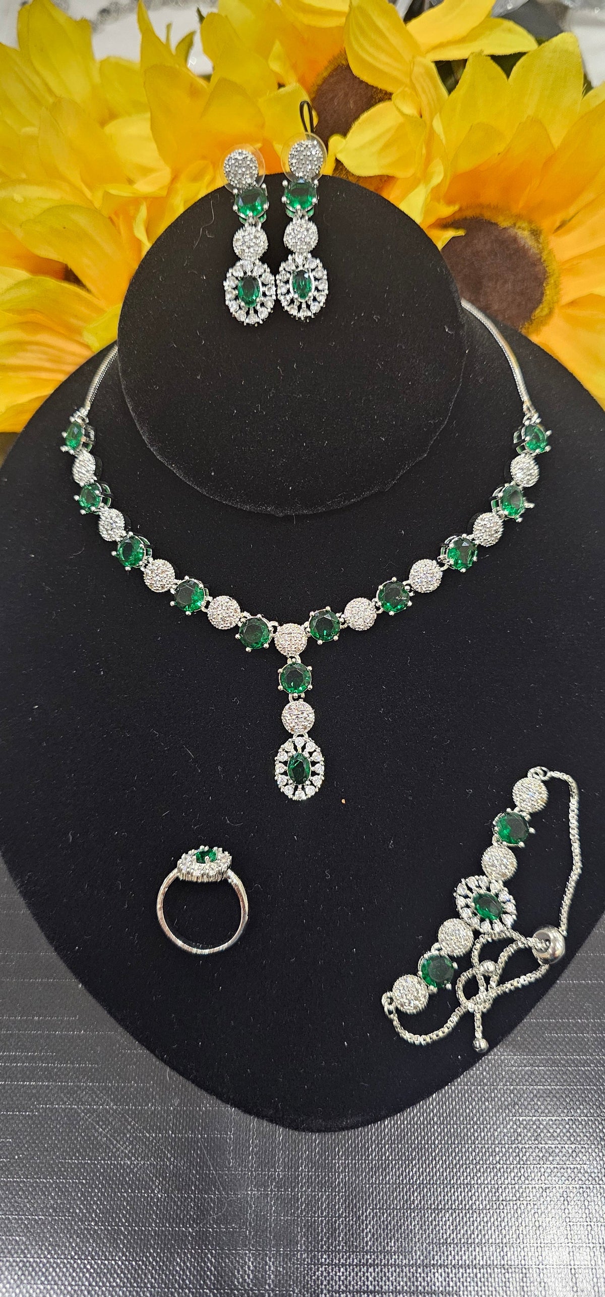 Green necklace with alternating colored centers and clear clusters with a central drop, shown with coordinating jewelry.