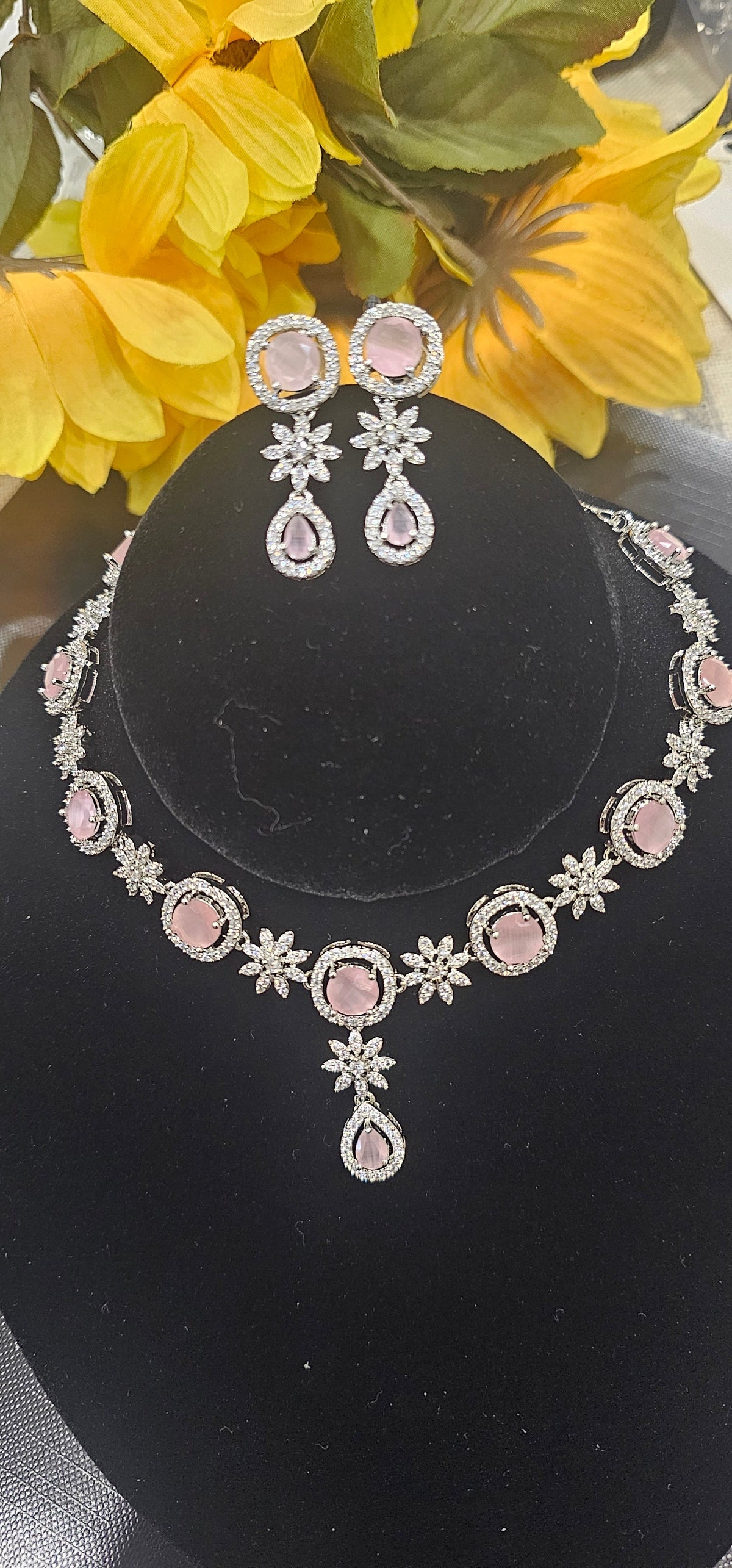 PINK necklace with oval colored accents alternating with clear flower-shaped links and a teardrop drop, shown with coordinating jewelry.