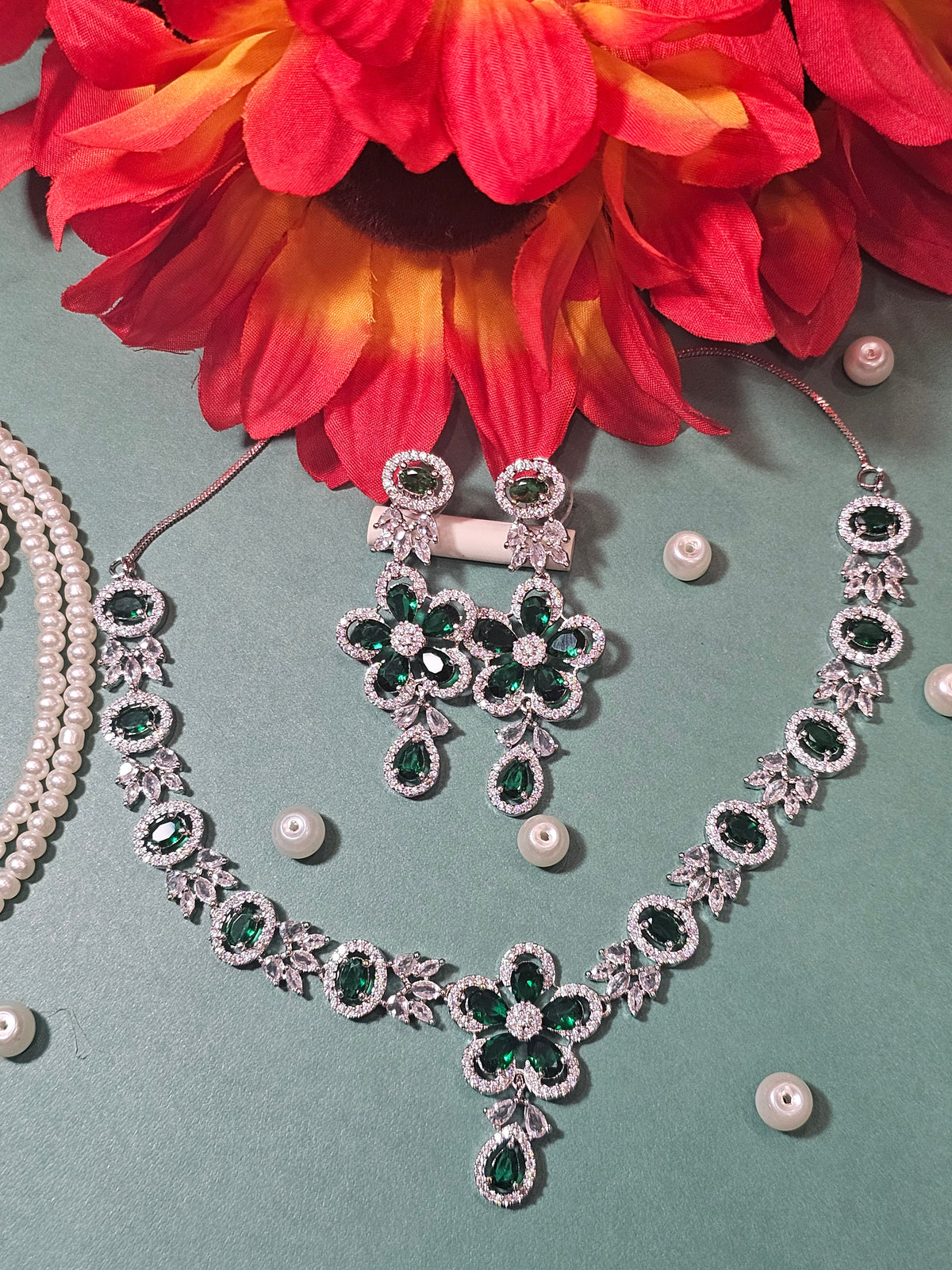 Green necklace with a flower-shaped pendant, oval colored accents and a teardrop drop, shown with coordinating jewelry.