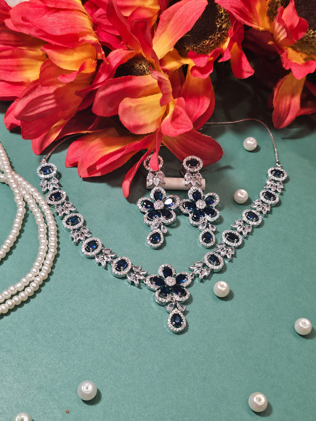 Navy necklace with a flower-shaped pendant, oval colored accents and a teardrop drop, shown with coordinating jewelry.
