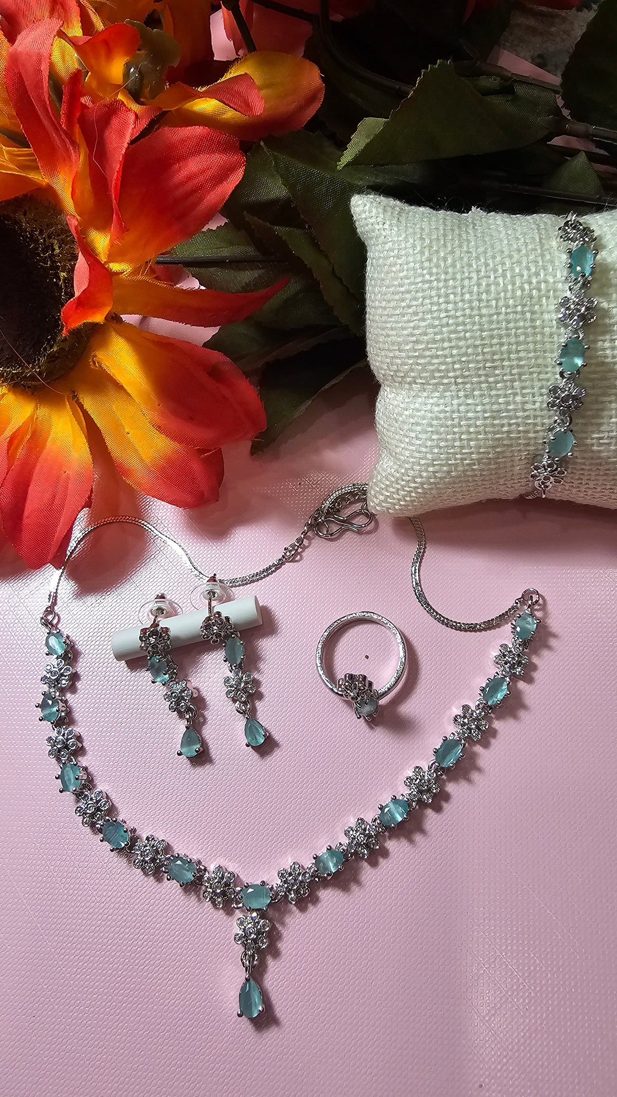 mint green necklace with alternating colored accents and small clear flower-shaped links with a central drop, shown with coordinating jewelry.