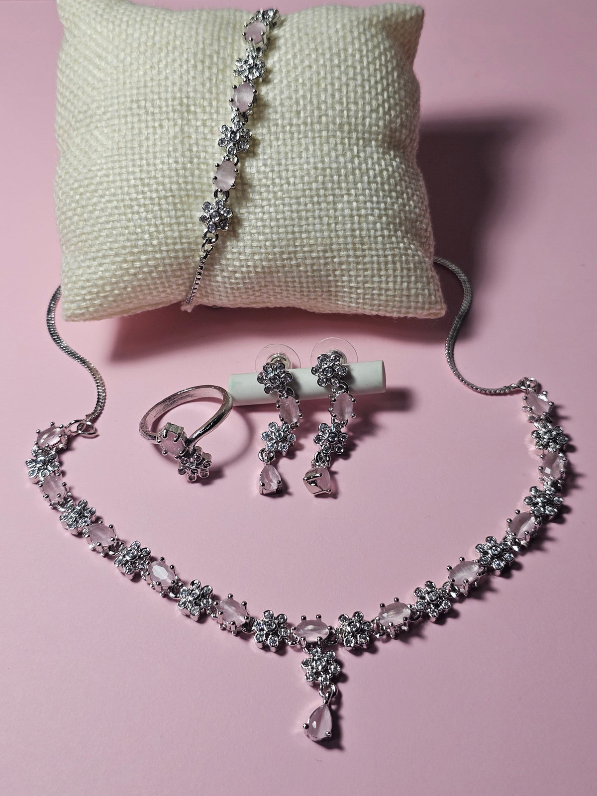 baby pink necklace with alternating colored accents and small clear flower-shaped links with a central drop, shown with coordinating jewelry.
