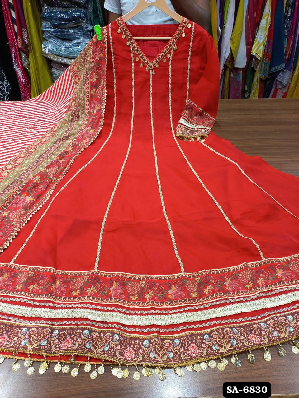 Red flared Anarkali dress with vertical trim and a wide floral border, photographed with a coordinating drape.