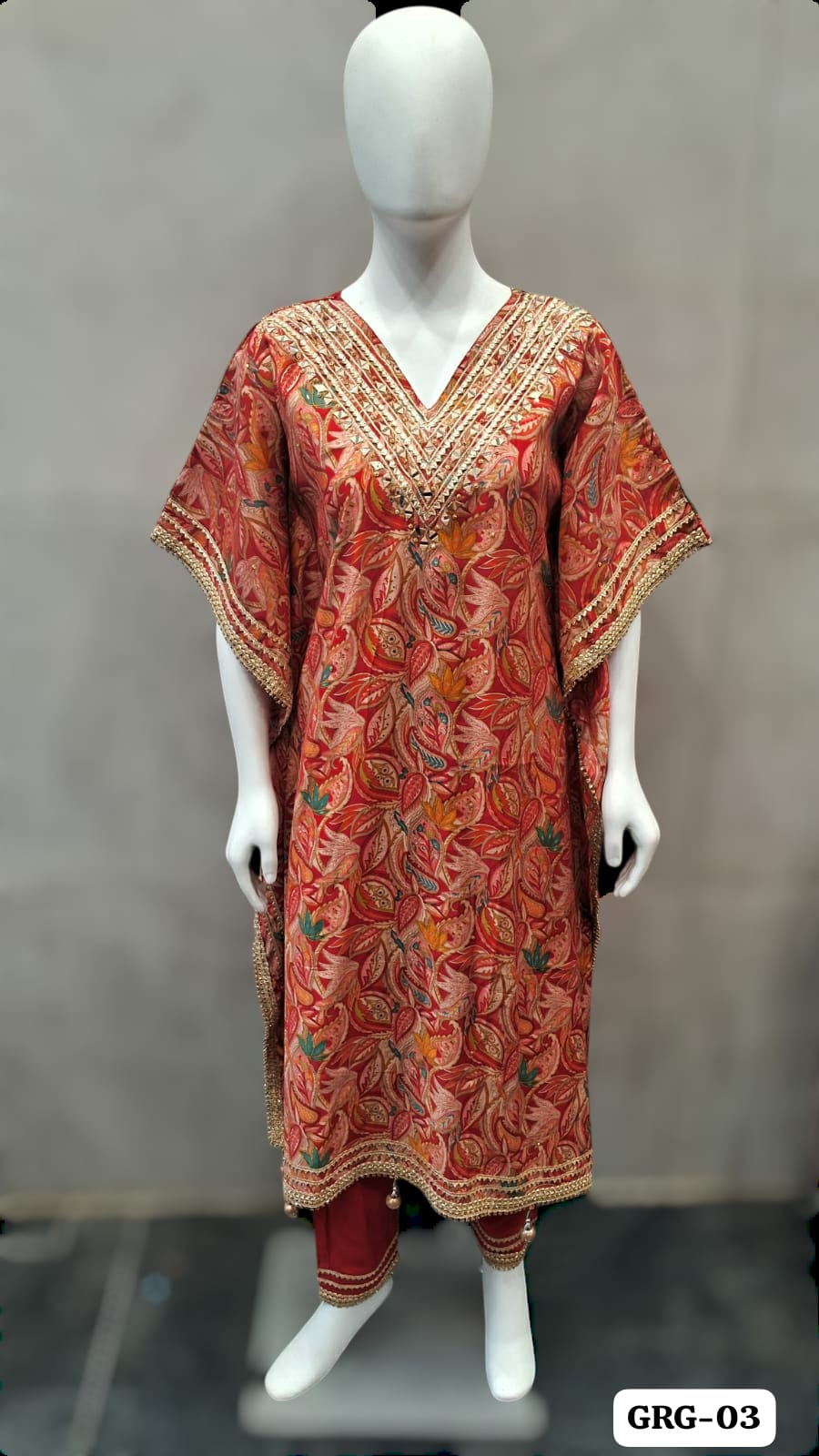 Rust Red kaftan with multicolor leaf motifs, wide sleeves and a trimmed V-neckline, shown on a mannequin.