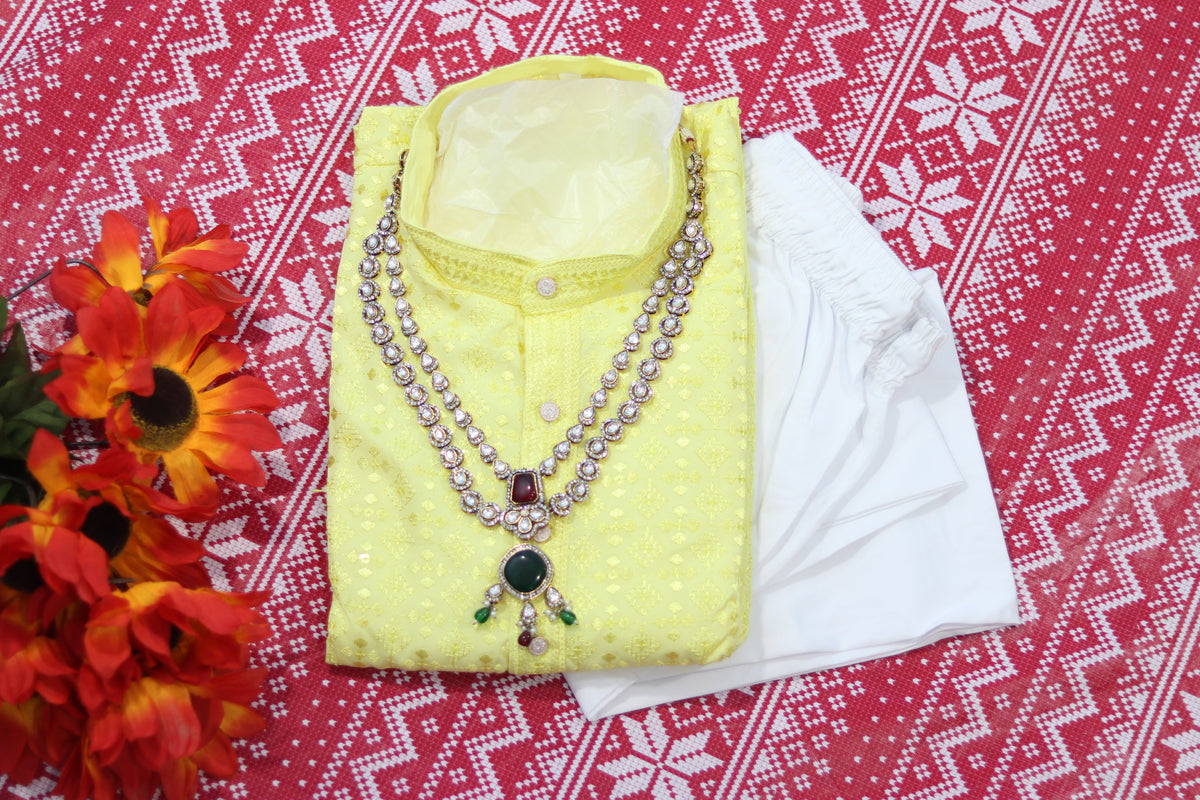 Folded lemon yellow kurta with repeating motifs, a band collar and front buttons, arranged beside white fabric and decorative flowers.