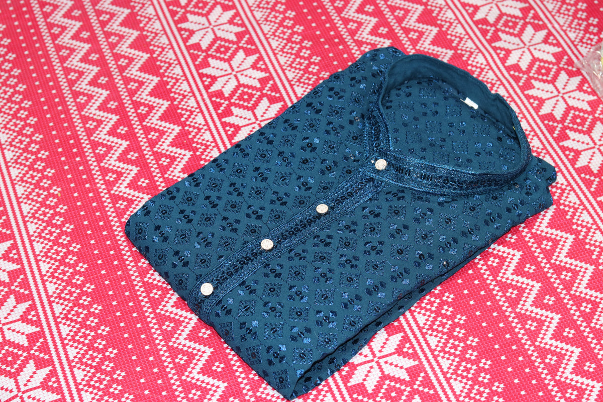 Folded teal blue kurta with small geometric motifs, a band collar and front buttons, arranged beside white fabric and decorative flowers.