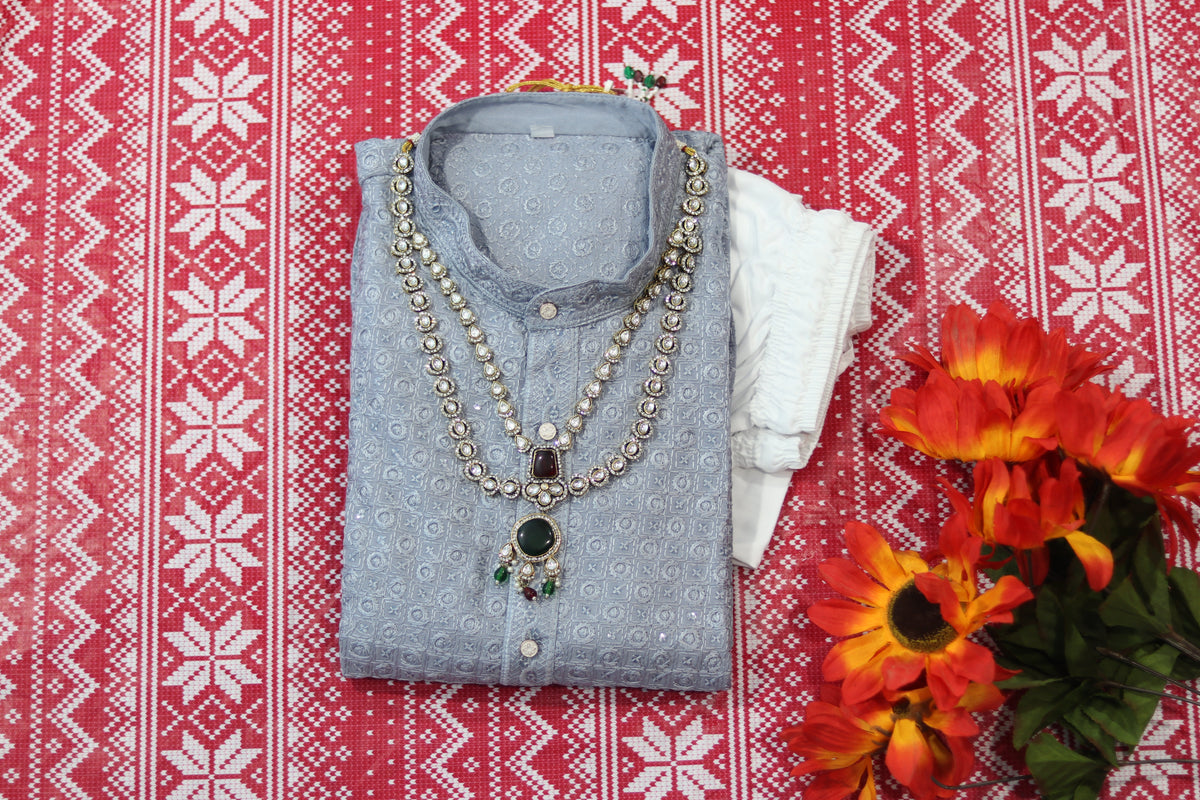 Folded silver grey kurta with small circular motifs, a band collar and front buttons, arranged beside white fabric and decorative flowers.