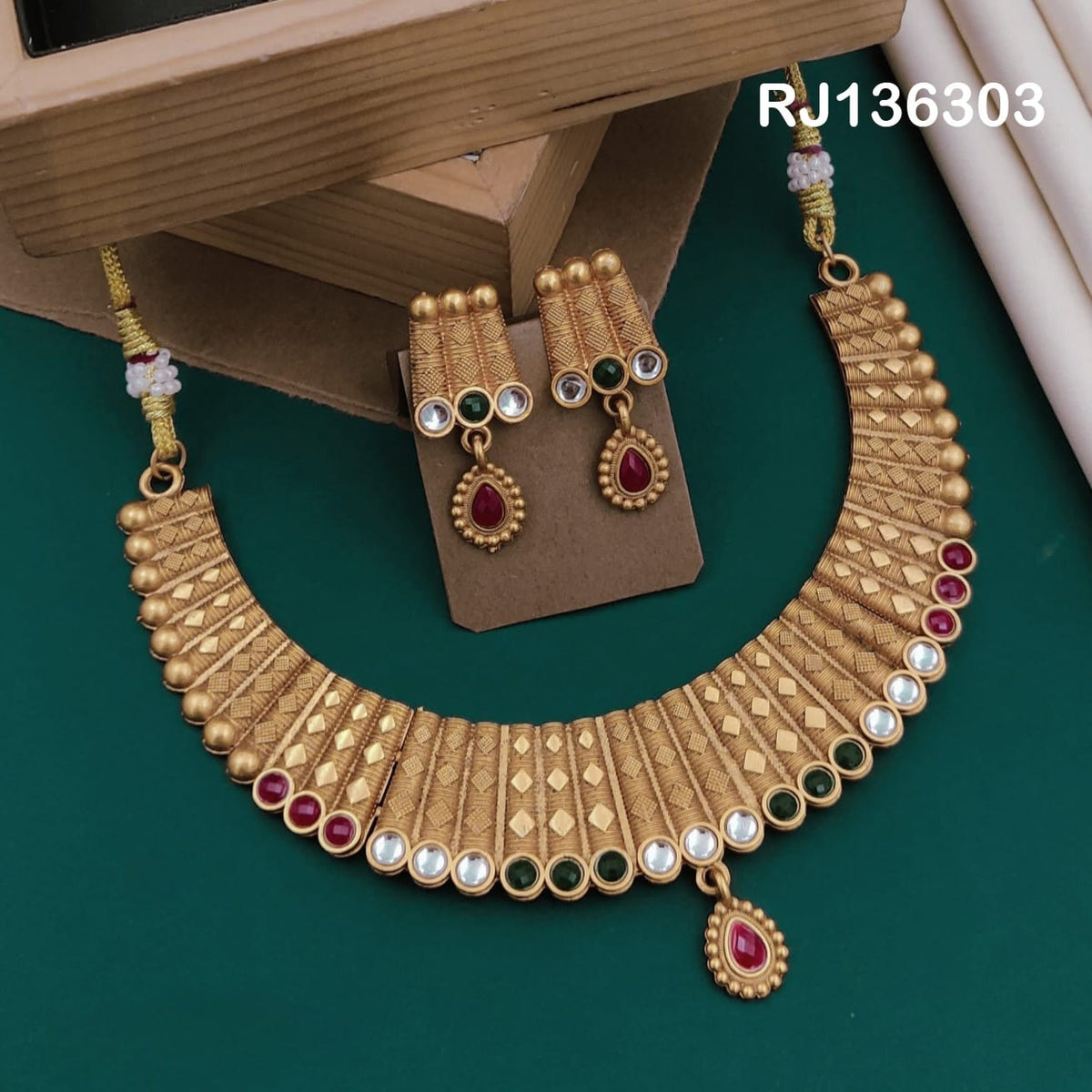 Antique gold-tone necklace with textured tapered panels, a border of red, green and white accents and a red drop, shown with coordinating drop earrings.