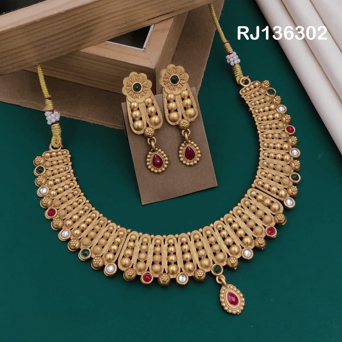 Antique gold-tone necklace with rows of looped textured details, rounded beads and a red teardrop accent, shown with coordinating drop earrings.