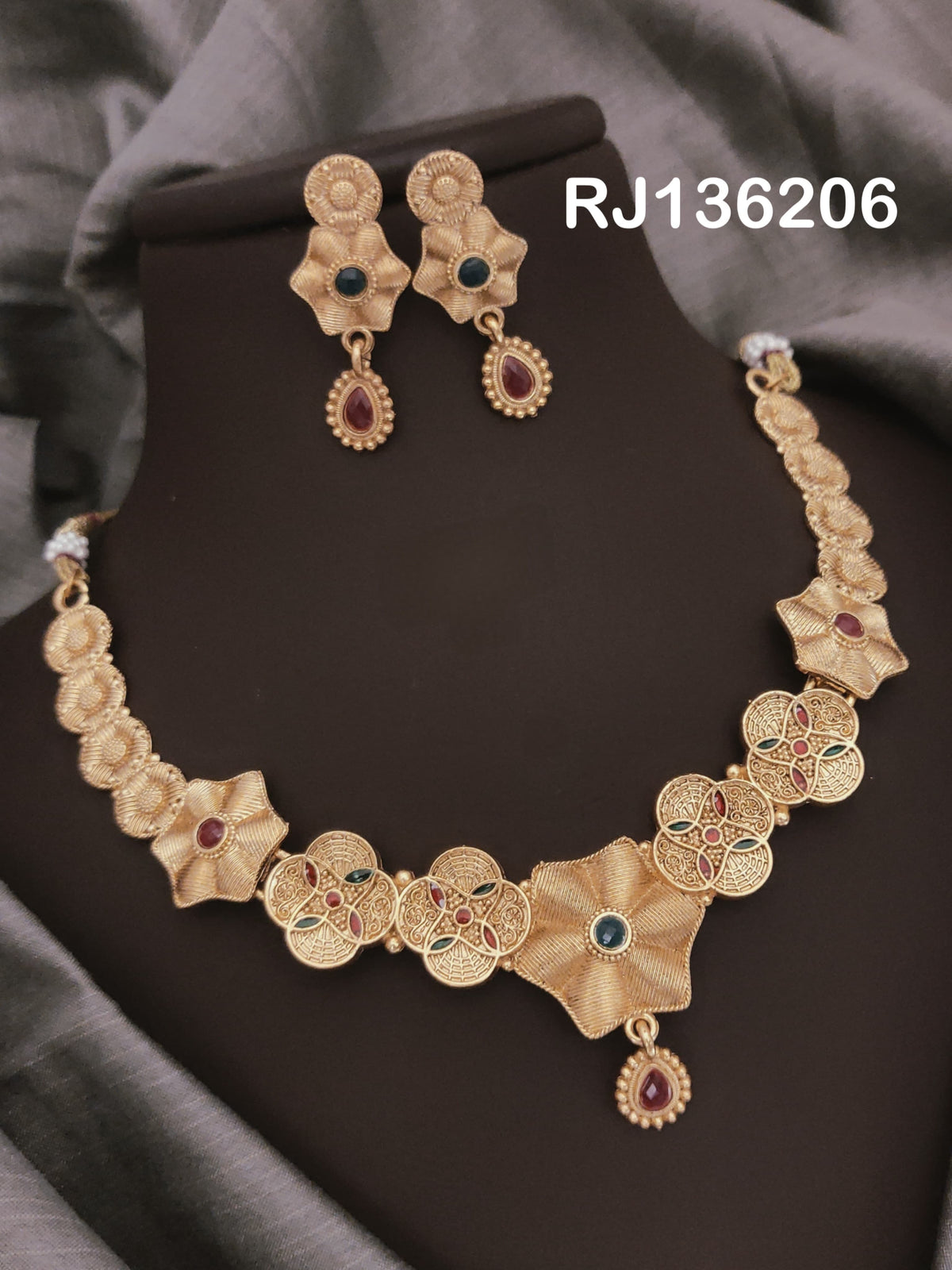 Antique gold-tone necklace with openwork four-petal flowers alternating with softly folded flower shapes and a red drop, shown with coordinating drop earrings.