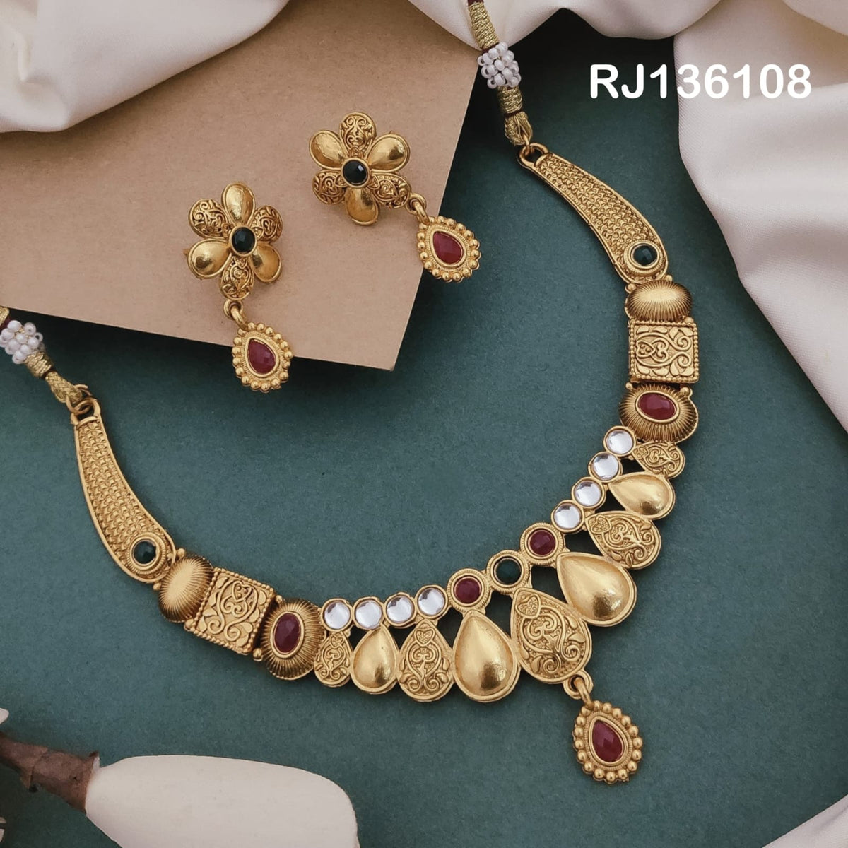 Antique gold-tone necklace with alternating smooth and patterned teardrop motifs, colored round accents and a central red drop, shown with coordinating drop earrings.